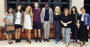 Nine adults, a mix of teachers and students, stand side by side and pose for a photo.