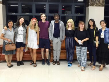 Nine adults, a mix of teachers and students, stand side by side and pose for a photo.
