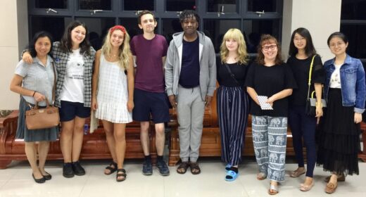 Nine adults, a mix of teachers and students, stand side by side and pose for a photo.