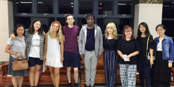 Nine adults, a mix of teachers and students, stand side by side and pose for a photo.