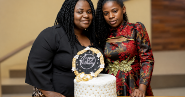 Two women stand together in front of a cake with a 