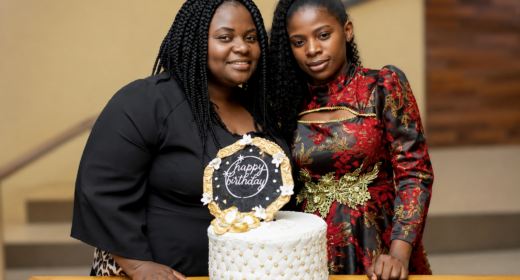 Two women stand together in front of a cake with a 
