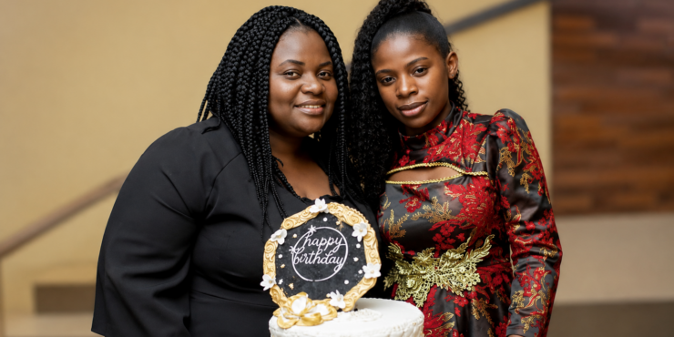 Two women stand together in front of a cake with a